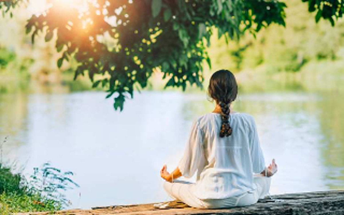 A woman meditating peacefully beside a calm lake at sunset